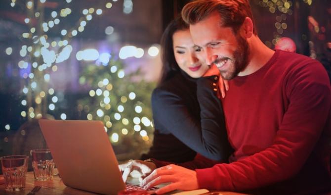 мъж и жена стоят пред лаптоп усмихнати